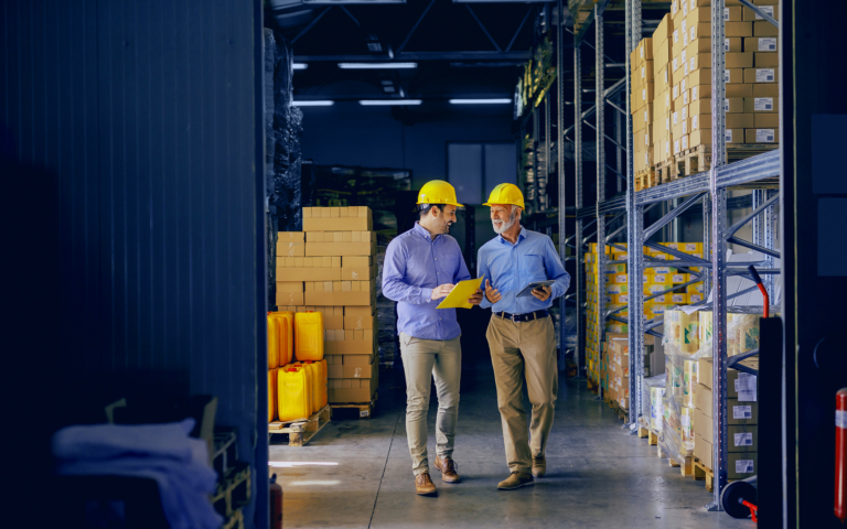 Coworkers Walking Through Warehouse With Paperwork