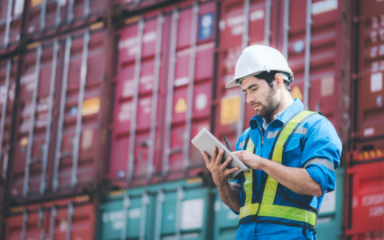Dock worker checking a tablet by containers